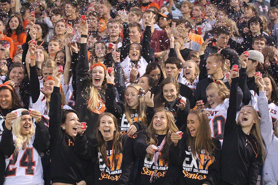 Throwing+confetti+in+the+air%2C+the+student+section+cheers+as+the+football+players+run+out+for+the+homecoming+game.+The+theme+for+homecoming+was+orange+and+black.+