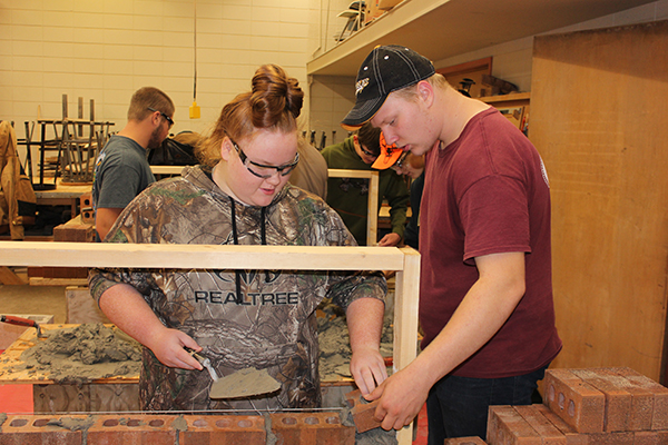 Using teamwork, sophomore Madison Shontz and senior Alex White practice spreading mortar and laying brick in Basic Carpentry. SMI taught students how they do their jobs and then let students do it themselves. 