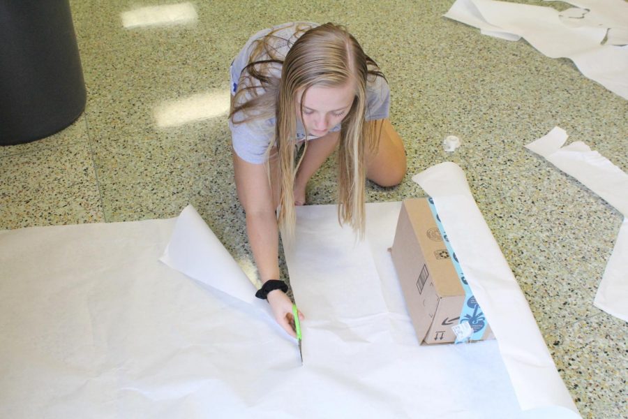 Wrapping a present for the Winter- themed hallway, sophomore Kylinne Meyers cuts off a piece of white paper at homecoming decorating.
