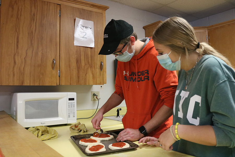 Lukas Meyer and Kylinne Meyers spread pizza sauce on the dough and add the toppings.