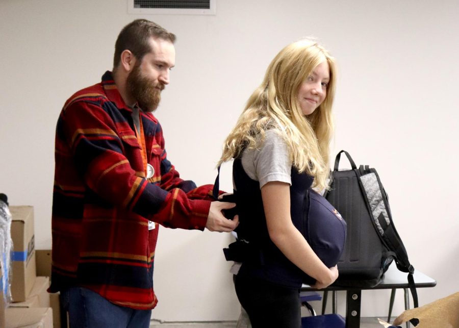 Teacher Christian Carper assists Isabelle Demmer (9) in putting on the empathy belly. 