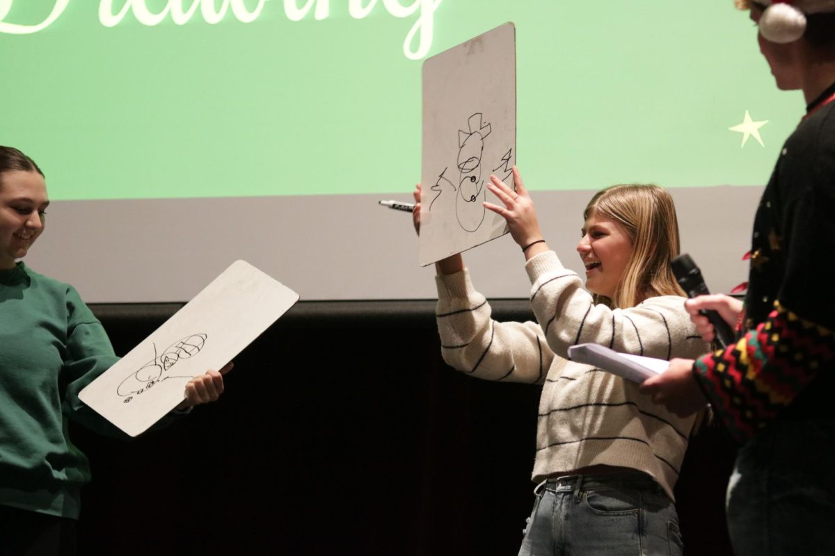 Sophomore Rayleigh Heims presents her artwork to the crowd. The goal of the game was to draw a prompt while the whiteboard was placed on your head.