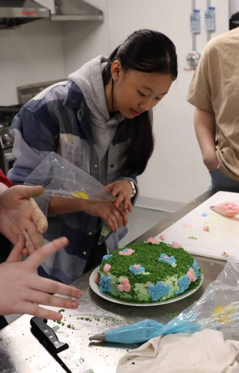Adding the last few flowers, Meagan Tran (12) helps her group decorate their cake with homemade frosting and crumbles of green cake.