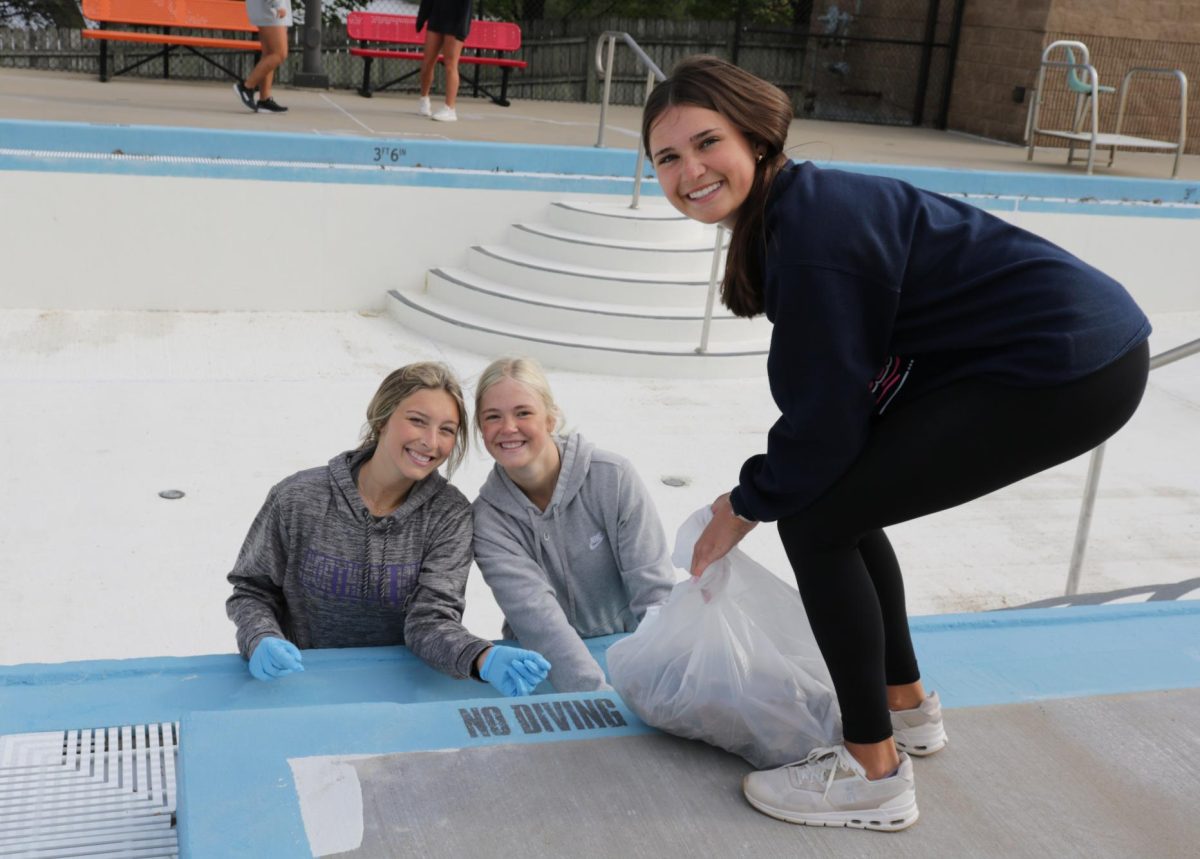 Seniors Taylor Domeyer, Kyria Loecke, and Emma Hogan smile while unclogging drains at the Manchester Aquatic Center during senior service day. They also helped pick up trash in the empty pools and scrub waterslides.