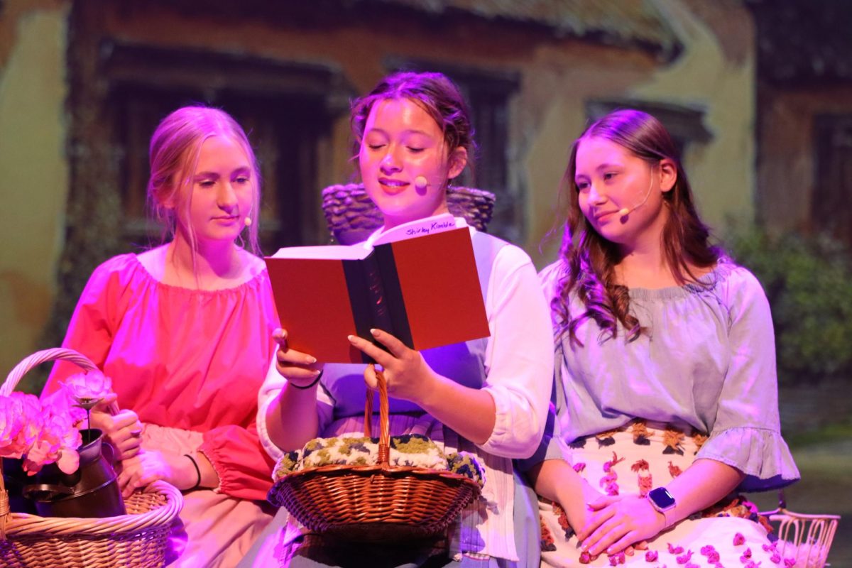 Early in the musical, Grace Sleper as Belle reads while villagers Gwenyth Hough and Addisyn Kintzle listen. 