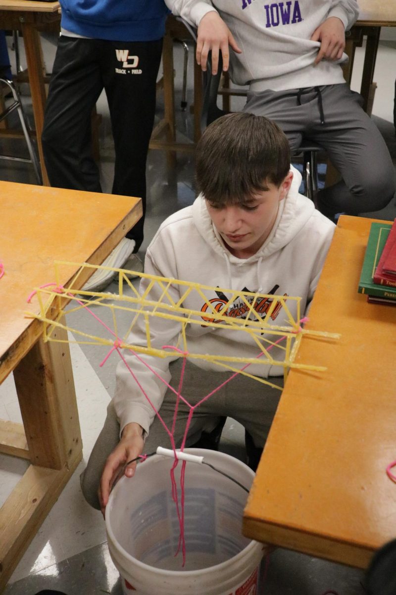With steady hands, Lance Feldman (11) balances the bucket as he prepares to add weight. "This experiment taught us the basics of engineering and architecture," Feldman said. 