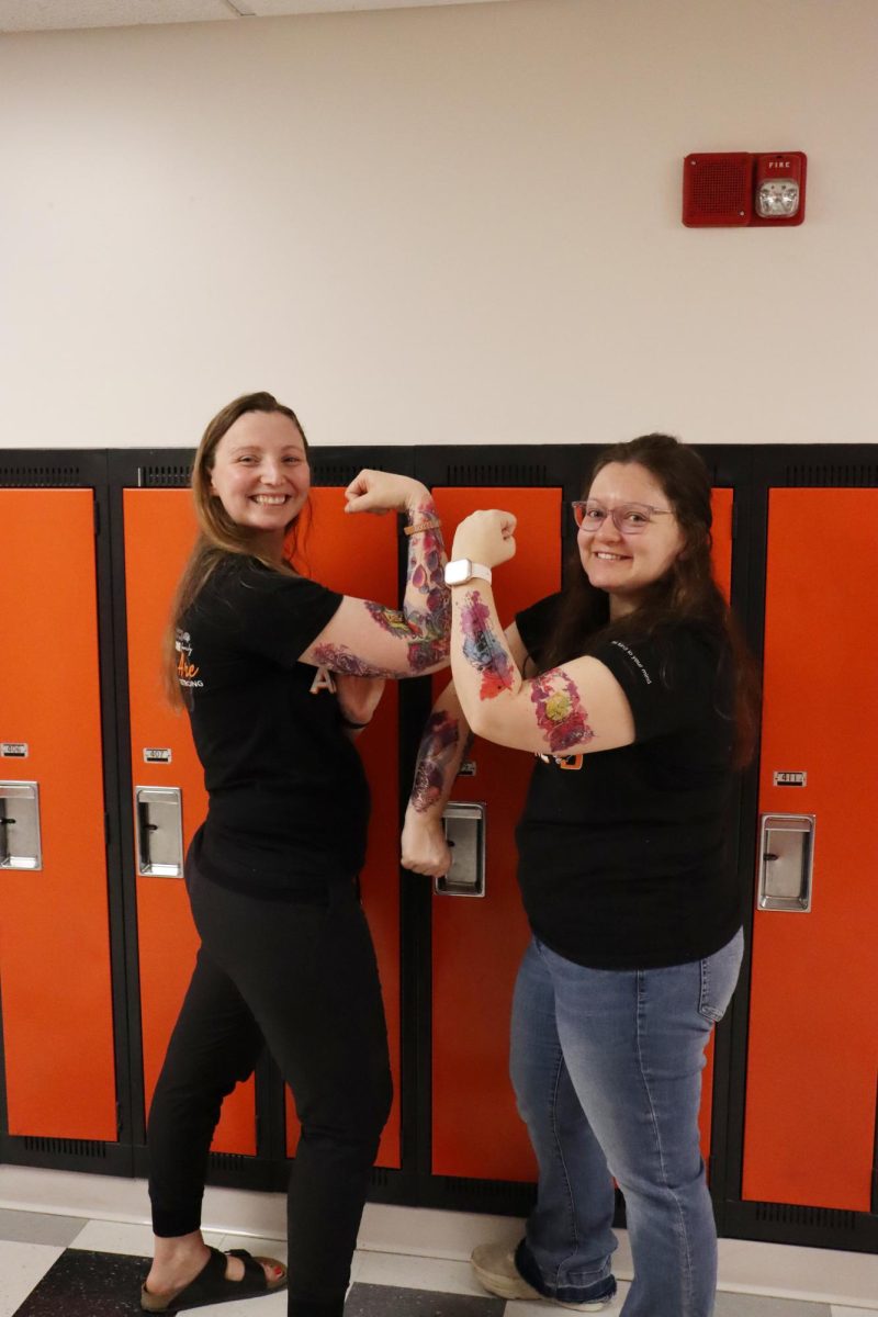 Posing for their picture, teachers Jennie Seabold and Abigail Goldsmith flex their tattoos to the camera.