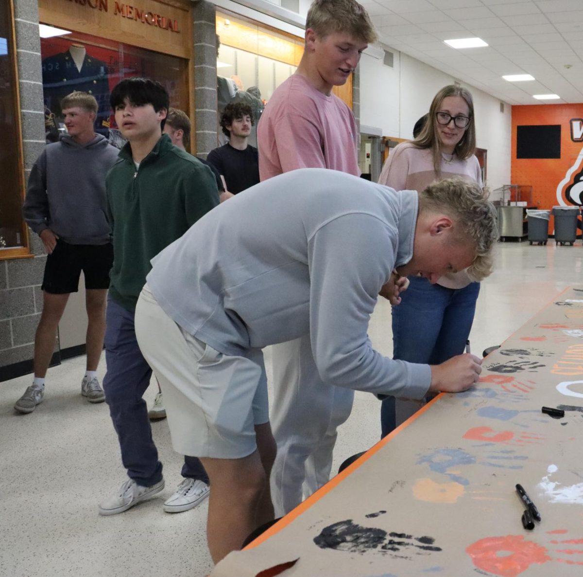 During his last homeroom, Austin Schnieders (12) signs his name on the banner.