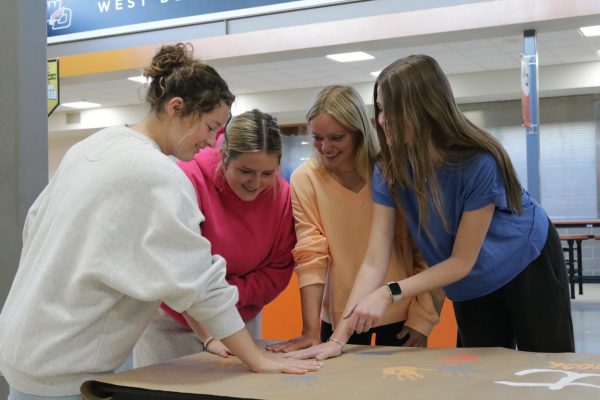 Having fun, Grace Sleper (12), Reagan Reeder (12), Brooklin Ante (12) and Alaina Bardgett (12) press their hands on the banner together.
